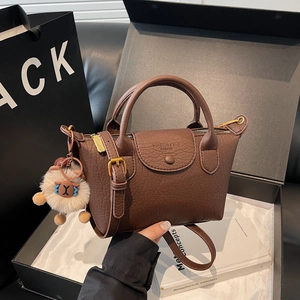 Braune Tragetasche aus Leder mit Gold-Hardware und beigem Plüschanhänger im Lifestyle-Stil