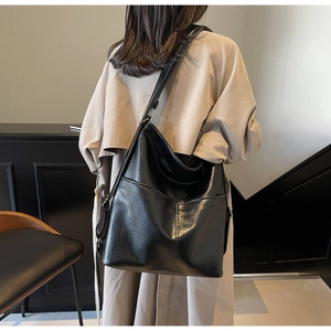 Rückansicht eines Models mit großer schwarzer Retro-Umhängetasche aus Leder und Trenchcoat