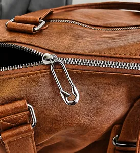 Close-up of brown textured leather bag with creative silver safety pin zipper detail