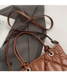 Détail du sac seau en cuir matelassé marron avec poignée nouée et œillets argentés