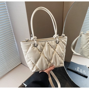 Détail du sac matelassé beige avec doubles poignées et bandoulière porté à la main