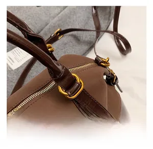 Detail der mattbraunen Ledertasche mit goldenem Dreieckslogo und polierten Beschlägen