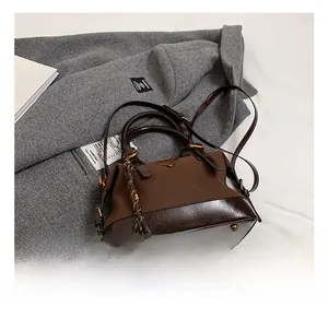 Detailansicht der dunkelbraunen Lederhandtasche mit Metall-Logo auf einem Wollmantel