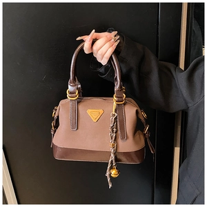 Detail einer braunen Patchwork-Handtasche mit dreieckigem Logo und gewebtem Trageriemen