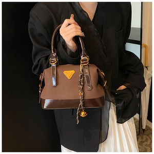 Detail der Handtasche mit Farbblock-Design, Goldbeschlägen und gewebtem Anhänger