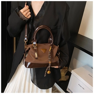 Detail der dunkelbraunen Handtasche mit Lacklederbesatz und goldenem Kugelanhänger