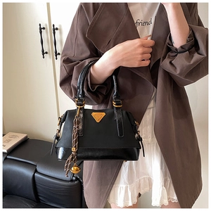 Details der schwarzen Handtasche mit goldenem Dreieck-Logo und gewebtem Quasten-Anhänger