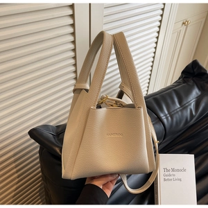 Detail of beige litchi grain leather bucket bag with top handle and logo on a black sofa