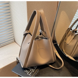 Detail of lychee pattern leather bucket bag with gold KAMIROO logo on grey surface