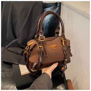 Detail einer braunen Boston Bag mit gestepptem Leder und einem goldenen Dreieck-Emblem