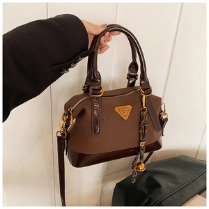 Detailansicht der braunen Handtasche mit goldenem Logo und geflochtenem Anhänger-Detail