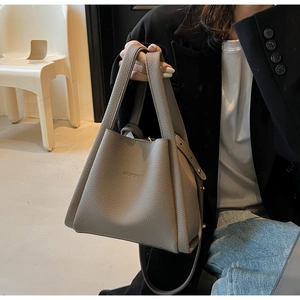 Detail of grey lychee leather bucket bag showing dual handles and gold-tone hardware