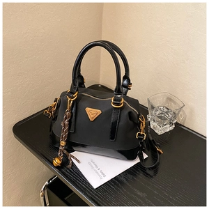 Detail der schwarzen Nylon- und Lackledertasche mit Goldbeschlägen und Logo-Dreieck