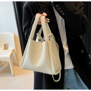 Close-up of minimalist cream tote bag showing pebbled leather texture and embossed logo