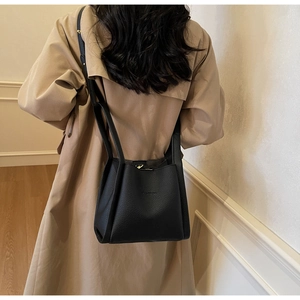 Rear view of a model wearing a black lychee-grain leather bucket bag with a beige trench coat