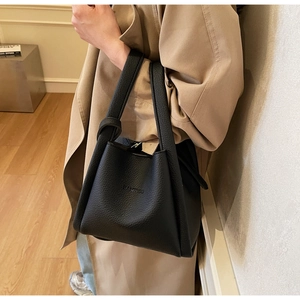 Detail of black lychee-textured leather bucket bag with embossed logo on the front