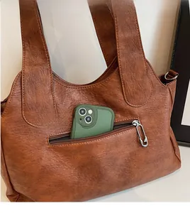 Detail einer braunen Shopper-Tasche mit Reißverschlusstasche und Metall-Clip-Zieher aus Leder