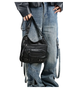 Detail of vintage black washed leather crossbody bag with punk style zippers and metal studs