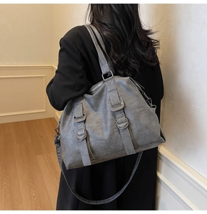 Rear view of a textured grey tote bag worn by a model, showing straps and metal hardware