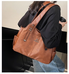Detail of a large brown leather tote bag with a kangaroo metal logo and side pockets