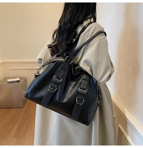 Détail d'un grand sac cabas noir avec texture litchi et boucles argentées porté par un modèle