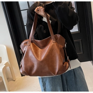 Close-up of brown leather tote bag showing lychee grain texture and metal side buckle