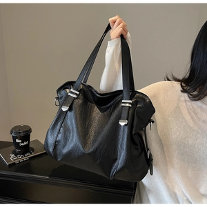 Close-up of large black tote bag with silver buckle details and textured faux leather