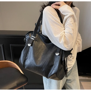 Close-up of a large black leather tote bag with silver hardware on a female model