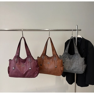 Close-up of three faux leather shoulder bags in burgundy, brown, and grey with metal logos