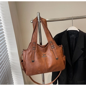 Detail of a brown leather tote bag featuring a kangaroo metal logo and lychee grain texture