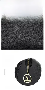 Close-up of black litchi grain leather texture and golden kangaroo metal pendant