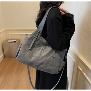 Detail of grey pebbled leather tote bag featuring a kangaroo metal logo and side pocket