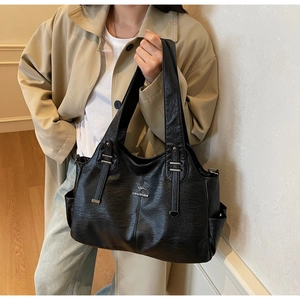 Detailed view of black faux leather tote bag with silver metal logo and side pocket