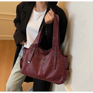 Detail of burgundy textured leather tote bag with metallic logo on a professional model