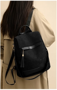 Detail view of black corduroy backpack featuring leather trim and long tassel on a model