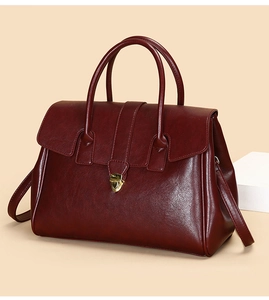 Detail of burgundy textured leather handbag with a gold heart-shaped metal clasp closure