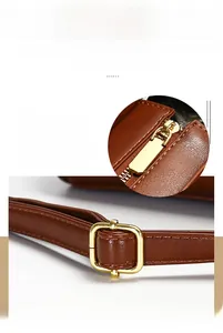 Detail of smooth gold zipper and adjustable metal buckle on brown leather tote bag