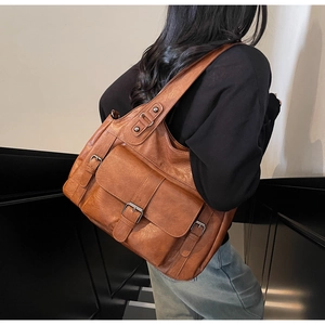 Detail view of large brown tote bag showing smooth leather texture and metal buckles