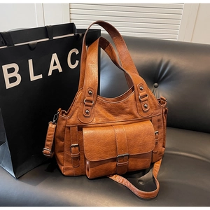 Close-up of vintage brown leather tote bag on a black sofa with decorative buckles
