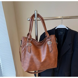 Close-up of brown faux leather tote bag showing fine texture and silver metal buckle
