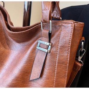 Close-up of brown litchi pattern leather and silver metallic hardware on a tote bag