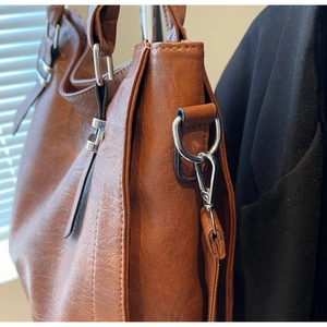Detail shot of brown leather tote bag with silver metal hooks and premium texture
