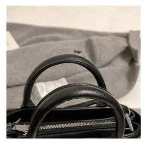 Détail d'un sac à main en cuir noir avec doubles anses rondes et fermeture éclair argentée