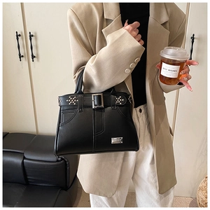 Détail du sac à main en cuir noir avec clous argentés et boucle de ceinture sur modèle