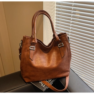Detail of caramel brown tote bag with leather texture and silver buckle on a chair