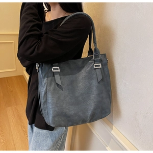 Detailed view of gray-blue faux leather tote bag with metal buckle on a shoulder strap