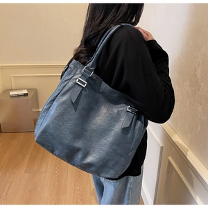 Detail of blue-grey tote bag with dual shoulder straps and metallic buckle on leather