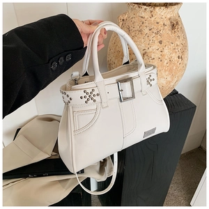 Détail d'un sac à main crème avec rivets métalliques et accents de ceinture