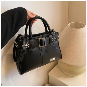 Détail du sac à main en cuir noir avec boucle argentée, clous et plaque de logo en métal