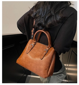 Caramel brown leather tote bag worn as a shoulder bag against a modern dark background